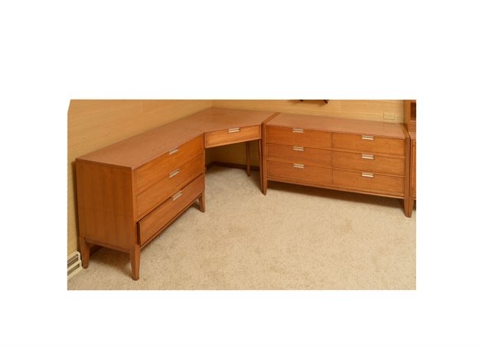 Mid Century Modern Walnut Corner Desk with Two Chests by Basic Witz: A Mid Century Modern walnut corner desk with two chests by Basic Witz. The top surfaces of all three pieces feature grained laminate over walnut cases with cross-banded veneer trimmed drawers. The drawers are fitted with silver-toned metal pulls and the cases rest on tapered legs. One chest has three drawers and the other, six. 
The corner desk rises on four straight legs to bring it to the same height as the two chests. A drawer is marked to the interior with the “Basic-Witz Waynesboro, Va” logo. Matching piece listed under 17CHI183-006.