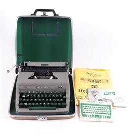 Royal Quiet De Luxe Typewriter: A Royal Quiet De Luxe typewriter. The typewriter has a taupe color with green keys on the keyboard. Included is a brown hard carrying case.
