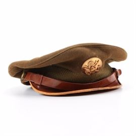 World War II Army Air Corp Hat: A World War II U.S. Army Air Corp hat. This circa 1944 visor hat features a brown leather visor, a band of olive colored canvas is surrounded by a strip of sizing leather, and is topped with a woolen beret style cap. The cap is embellished with a circular gold toned metal medallion depicting a crest, an eagle with spread wings, and a banner reading “E Pluribus Unum”.