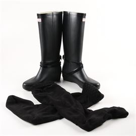 Hunter "Andora" Wedge Rain Boots and Boot Socks: A pair of Hunter Andora wedge rain boots. The black rubber boots, size 9, feature crisscross ankle straps and labelled branding on the strap buckles, front shafts, interior textile linings, and soles. The boots are presented with a pair of Hunter brand black fleece boot socks.