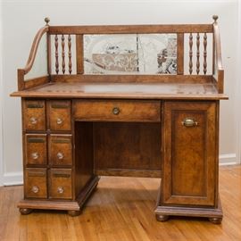 Double Pedestal Desk: A double pedestal desk. This desk features a rectangular top with inset leather flanked by sloped edges to each side and a raised back with mirrored panel to center flanked by turned spindles to each side. The top rests over a center drawer above a kneehole flanked by a cabinet to one side and a set of three drawers to another that rise above a molded edge base terminating on bun feet.