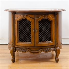 Vintage Pecan Round Side Table: A vintage pecan round side table featuring a veneered top with a routed and scalloped edge over a round case. The case is fitted with arched cabinet doors with carved scrolled details and metal mesh inserts. The rounded sides are veneered and the piece stands on four cabriole legs terminating on whorl feet joined by a carved apron with scrolled details. Matching table listed unde