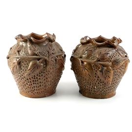 Brown Ceramic Vase: A set of two brown ceramic vases. The matching vases have wavy rims, a raised leaf design around the rounded shoulders and an all over triangular textured pattern on the tapered bodies.