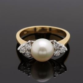18K Yellow Gold Cultured Pearl and Diamond Ring: An 18K yellow gold cultured pearl and diamond ring. This ring features a white gold setting housing a center cultured pearl placed between diamond trios leading to a yellow gold shank.