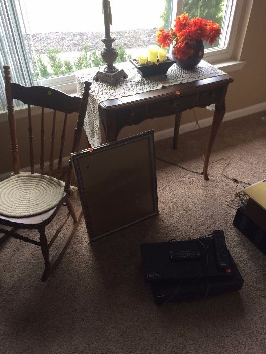 old rocking chair.  VHS player, Blu Ray DVD player, antique table, lamp, candlers, flower vase