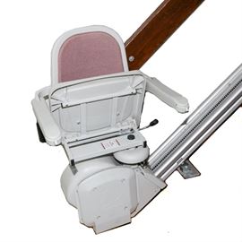 Acorn Stair Lift: An Acorn stair lift. This electric chair lift features a padded armchair with a seat belt, a 12-foot track, and a backup battery in case of power outage. It is presented with keys and a remote control.