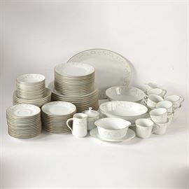 Noritake "Duetto" Tableware: A selection of Noritake Duetto tableware. This set includes two platters in different sizes, twelve soup bowls, twelve cereal bowls, one round vegetable bowl, one oval vegetable bowl, twelve dinner plates, twelve salad plates, twelve bread and butter plates, one gravy boat with drip tray, one creamer, one lidded sugar bowl, thirteen teacups, and fourteen saucers featuring a gold and white scrolling design with gilt trim. Each piece is marked “Noritake Japan 6610 Duetto Japan”