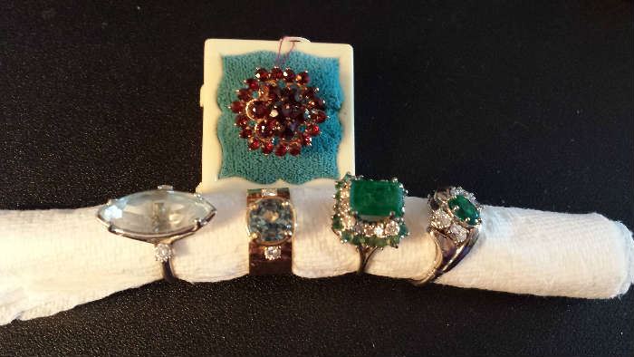 Left to right: Light blue topaz, diamond and medium color blue topaz, emerald and diamond, emerald and diamond, garnet cluster in back.