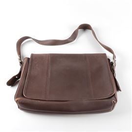 Brown leather Coach Bag: A brown leather Coach bag. The bag is a parcel style with a front flap with leather piping and a zippered compartment. The bag has a leather strap with a silver-tone buckle on both sides, a brown suede interior with compartments and a leather plaque with the Coach creed.