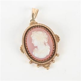14K Gold and Cameo Pendant Brooch: A 14K yellow gold and shell cameo pendant-brooch. The coral colored carved shell cameo depicts an elegant bust of a women in side profile, held in a prong setting with an ornate bezel, featuring foliage and bead ornamentation, with a safety clasp attached on the verso, and a pendant loop at the top. No discernible maker’s marks were found.