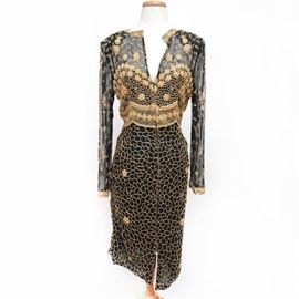 Vintage Neiman Marcus Beaded Gold-Tone and Black Silk Dress: A vintage Neiman Marcus Beaded gold-tone and black silk dress. Comprised of a delicate see-through decolletage and sleeves, this dress features a straight skirt with a partially open lower central edge. This dress features an intricate beaded golden-tone floral motif and a gadroon waist line. To the top center of the interior a “Neiman Marcus” tag with an underlying “Judith Ann Collections, made in India” are affixed.