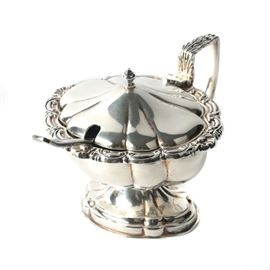 Israel Freeman & Son English Silver Plated Mustard Pot: An English silver plate mustard pot by Israel Freeman & Son. This features a domed hinged lid over a scroll rimmed lobed body that rises on a flaring pedestal base with a foliate angular handle. It is marked underneath “Made in England” with a pictorial makers mark. This has a cobalt blue glass lining and a diminutive condiment spoon by J.B Ltd of Sheffield.