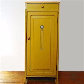 Art Deco Cabinet from Oscar Onken: An Art Deco painted cabinet from The Oscar Onken Co. of Cincinnati, Ohio. The narrow cabinet is painted in a yellow gold, with a single top divided-interior drawer with a gold bakelite pull and paneled door with an Art Deco stenciled motif to the center. The cabinet has two fixed shelves to the interior. The cabinet has flat panel sides and applied curved feet.