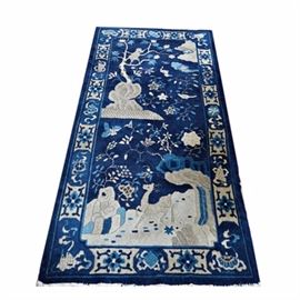 Semi-Antique Handwoven Chinese Wool Accent Rug: A semi-antique handwoven Chinese wool accent rug. The rug has a navy blue background populated with flowering trees and flying birds in shades of ecru, off white and medium blue. To the top of the field in a money in a flowering lotus tree, with a cloud formation to the upper right corner, the tree rising up from a rock formation. To the bottom of the rug’s field in a landscape with stag and rock formations. The rug has a major border with ecru medallions filled with blue flowers, alternating with traditional Chinese motifs and arabesque forms. The rug is finished to both ends with off white warp fringe.
