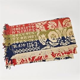 Signed 1853 Handwoven Wool Coverlet: A signed 1853 handwoven wool coverlet. The coverlet was made by John Graham in 1853 in Morris Township, Knox County, Ohio. The coverlet has a dark cream background, with alternating floral bands in cream and navy and olive green and tomato red, with a scrolling vine and berry motif to the outside and a fringed border. The coverlet is signed and dated in a signature block.