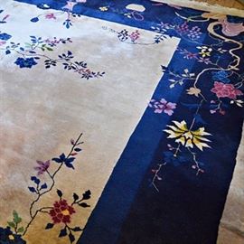 Semi-Antique Handwoven Chinese Wool Area Rug: A semi-antique handwoven Chinese wool area rug. The rug has a light ecru central field with wisteria, clematis and scrolling vine motifs, and bird accents, in shades of navy blue, celadon green, burgundy, lavender, yellow gold, raspberry and cream. The rug has a tonal navy blue border, also designed with floral decoration, including floral arrangement in vases. The rug is finished to both ends with off white warp fringe.