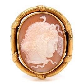 Victorian 14K Yellow Gold "Medusa" Cameo Brooch: A Victorian carved shell cameo brooch depicting the profile of Medusa with wings on her head and a pair of entwined snakes in the hair and at the throat. Medusa was one of the three Gorgons, transformed from a beautiful mortal woman as punishment by the goddess Athena for her dalliance with Poseidon. The 14K yellow gold oval mount has wrapped detailing and a hinged bar pin.