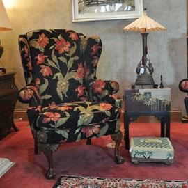 One of a pair of wing chairs with claw and ball front feet and heavily carved knees in very fine fabric, elephant lamp with paper umbrella shade (SOLD AT PREVIEW), petite trunk side table and petite point foot stool (retailed for $540)