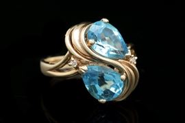 14K Yellow Gold, Blue Topaz and Diamond Ring: A 14K yellow gold, blue topaz and diamond ring. The ring features two prong set, pear shaped blue topaz set in an S-shaped curve of 14K yellow gold and accented to either side by two round brilliant cut diamonds.