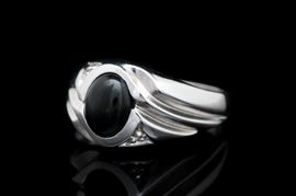 14K White Gold, Black Chalcedony and Diamond Ring: A 14K white gold, black chalcedony and diamond ring. The ring features a center set oval black chalcedony cabochon accented by two diamonds and ridged shoulders.