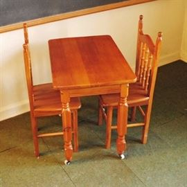 Vintage Child Size Pine Table and Chairs: A vintage stained pine child size table and chairs. The table has a rectangular top on turned legs, raised on casters. The two chairs have ball finials to the raised ears, and arched top rails over ball accented spindles on the backrest. They stand on block legs with offset box stretchers, accented to the front with two ball turns.