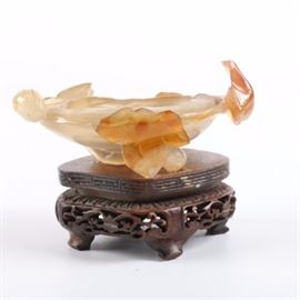 Chinese Carved Quartz Bowl: A Chinese carved quartz bowl on a carved mahogany base. The orange cream carnelian stone is carved into a roux bowl, with leaves wrapped around. The bowl comes with a carved wooden base, with an openwork design to the sides of the base.