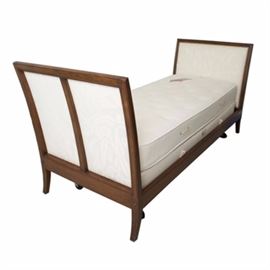 Regency Style Upholstered Day Bed: A Regency style upholstered day bed. This piece features a walnut stained frame and champagne hued upholstery in a foliate pattern, with nail head trim. It has flared head and footboards, and stands on square flared legs. Legs ending in casters are located beneath the mattress and box spring. There are no visible maker’s marks. For a coordinating piece, see item 17BOS186-124.