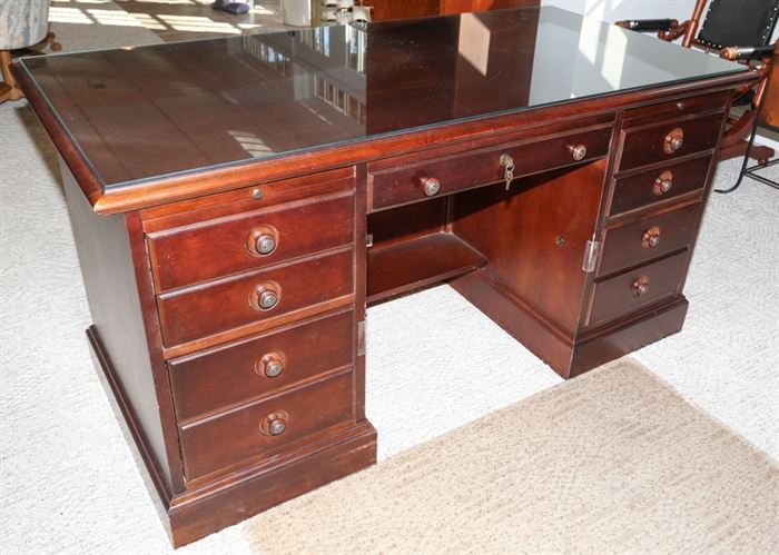 Executive Desk by Stanley Furniture: An executive style kneehole desk by Stanley Furniture. The desk features four drawers to both sides with circular pulls, a drawer to the center with key and a removable glass top. It is marked “Stanley Furniture” to the top left drawer.