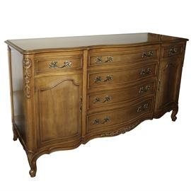 French Provincial Style Buffet: A French provincial style buffet. The buffet features intricate carved accents to the sides and the lower apron with floral and leaf detailing. There are six drawers in total with dovetail joinery and two doors to the sides with intricate handles with scroll style designs. There are no maker identifications. This item coordinates with items 17CLT177-033 and 17CLT177-035.