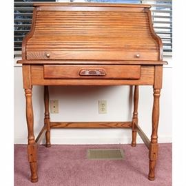 Secretary Style Oak Desk: A vintage oak roll top desk. This desk features a small shelf over a serpentine-shaped roll top opening to reveal four drawers flanking open cubbies and a desk surface. The base is fitted with a centered drawer with carved cup pull resting on four block and ring turned banister legs ending on peg feet joined by three straight stretchers.