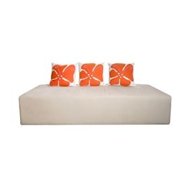 Modern Upholstered Bench with Accent Pillows: A contemporary Modern style upholstered bench with accent pillows. The bench is a rectangular, padded box shape completely upholstered in soft grey fabric rising on four short, round legs. Included are three square, felt pillows featuring graphic orange and pink flower forms on a white ground. The bench has no discernible maker’s mark and the pillows are tagged, “Hable Construction.”