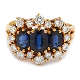 18K Yellow Gold Blue Sapphire and Diamond Ring: An 18K yellow gold blue sapphire and diamond ring. The ring features three oval sapphires with a diamond halo on a polished split shank.