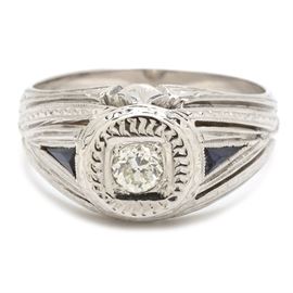 18K White Gold Diamond and Sapphire Ring: An 18K white gold diamond and sapphire milgrain ring. The ring features a European cut center diamond flanked by triangular blue sapphire accents in a vintage style setting.
