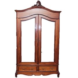 Antique Louis XV Style Mahogany Veneer Armoire: An antique Louis XV style armoire. This grand piece is constructed from walnut and oak with mahogany veneers, and it features a carved ornament on its domed top over beveled mirrors on the tall double doors opening to a spacious compartment. There are also two hand dovetailed drawers at base, and both doors and drawers have brass hardware. At the base is also a serpentine apron flanked by carved cabriole front feet.