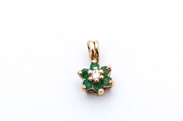 14K Yellow Gold Emerald and Diamond Pendant: A small 14K yellow gold flower shaped pendant with a round cut diamond prong set to the center of a halo of round cut emeralds.