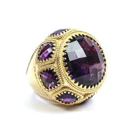 Rebecca Designer Gold Tone Ring with Purple Amethysts: A gold tone costume ring with checkerboard-cut purple amethyst gemstones, by Rebecca. The ring has a very wide shank and features a round center stone, surrounded by smaller stones, all in sawtooth bezel settings.