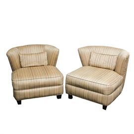 Pair of Custom Upholstered Lounge Chairs: A pair of custom upholstered, arm-less lounge chairs, each having a curved back with lumbar pillow and a tight seat and welted apron, covered on a beige, textured strie fabric. The chairs sit on four wooden feet.