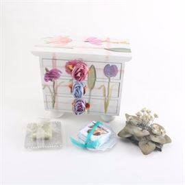 Assorted Vanity Décor: An assortment of vanity décor. Featured are a wooden jewelry box with a hand painted floral design, two sets of soaps with a soap dish, and a decorative ceramic floral accent. The items vary in style and maker.