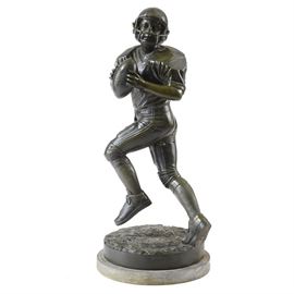 Large Scale Football Player Sculpture: A large-scale football player sculpture. This piece, constructed from a metal alloy, with an antique bronze finish, stands at three and a half feet tall and depicts a young football player running with the ball in his hand. He wears a Riddell helmet and a number 7 jersey. It is signed, in mold, by a company out of Thailand that uses the fictitious name “Jim Davidson.”