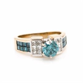 18K Yellow Gold 2.36 CTW Diamond Ring: An 18K yellow gold 2.36 ctw diamond ring. This ring showcases an irradiated blue diamond center, accented by twelve diamonds and twelve irradiated blue diamonds adorned to the ridged design shoulders.