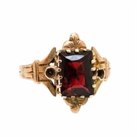 10K Yellow Gold Garnet Ring: A 10K yellow gold garnet ring. This ring showcases a garnet center adorned to the foliate designed crown, situated between flared and geometric designed shoulders.