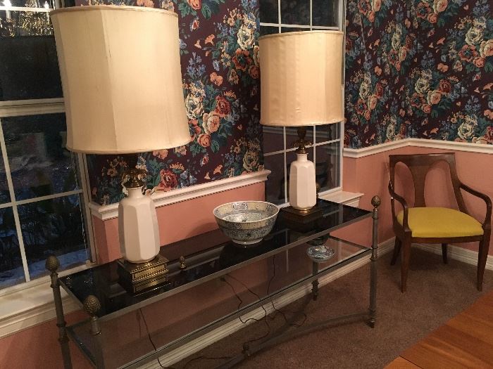 A 5 foot Glass, Metal and Brass Console table with pineapple finials pairing a smoked glass top with a lightly tinted glass shelf ; pair of Lenox Stiffel Porcelain and Brass lamps, 
