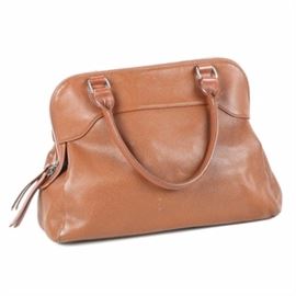 Longchamp Pebble Leather Handbag: A leather handbag by Longchamp. The bag is constructed with cognac colored pebble leather and has rolled handles, silver tone hardware, an exterior zip pocket, and a zip top closure. The bag’s roomy interior has a cognac colored logo lining with a zip pocket and patch pockets to the sides.