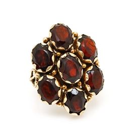 14K Yellow Gold 8.90 CTW Garnet Ring: A 14K yellow gold 8.90 ctw garnet ring. This ring features a scalloped oval center housing seven oval faceted garnet stones set between open textured shoulders.