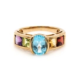 10K Yellow Gold Gemstone Ring: A 10K yellow gold gemstone ring. This ring features a center, half bezel set blue topaz stone that is flanked by channel set, citrine, garnet, peridot, and amethyst stones that lead to the high polish, tapered shoulders.