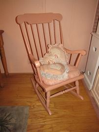 A wooden (with a cushion) rocking chair, painted pink.