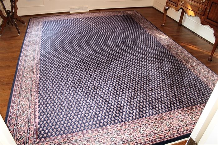 Machine Made Seraband-Style Area Rug: A large machine made Seraband-style area rug. The field is deep navy blue with a field of boteh forms, and the border features a Seraband pattern of rectangular layers of red, white, and blue patterns. It has serged edges and is partially tagged to the underside.