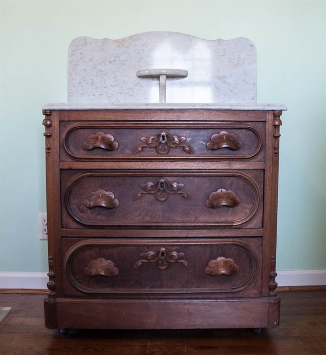 Victorian Marble Top Vanity Chest: A Victorian chest with a marble top with a marble backsplash and a small circular shelf. There are three drawers with fruit carved pulls and elliptical trim molding.