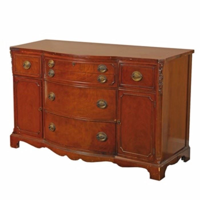 Vintage Empire Style Breakfront Cherry Cabinet: A vintage Empire style breakfront cherry cabinet having a rectangular top with a bowed front edge over a complaint case with four bowed drawers flanked by drawers over cabinets and carved foliate stiles. The drawer and cabinet shapes are accented with piping and brass embossed oval plates with bail handles. The top two drawers in the center are felt lined and fashioned to hold flatware. The piece rises on bracket feet joined by a compliant scalloped apron. No discernible maker’s mark.
