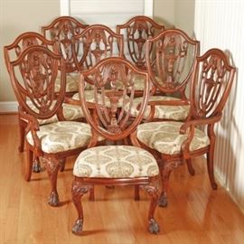 Vintage Hepplewhite Style Mahogany Dining Chairs: A set of eight vintage Hepplewhite style, mahogany dining chairs. The set includes two armchairs and six sides, all having shield shaped backs with festoon splats over upholstered slip seats and rising on Chippendale style cabriole legs with scroll carved knees and paw feet in the front and two splayed legs in the back. The padded seats are upholstered in a cream and avocado green paisley print. The armchairs share all these features plus curved and routed arms ending in scrolled handholds and supported by curved rails embellished with carved acanthus leaves. The chairs have no discernible maker’s mark.